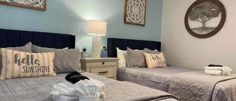 A bedroom with two beds, a nightstand, a lamp, and decorative wall art.
