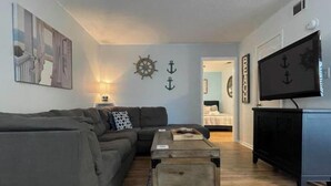 Ein Wohnzimmer mit einer Couch, einem Couchtisch und einem Fernseher. An den Wänden befinden sich Dekorationen, darunter ein Schiffsschwengel und Anker.