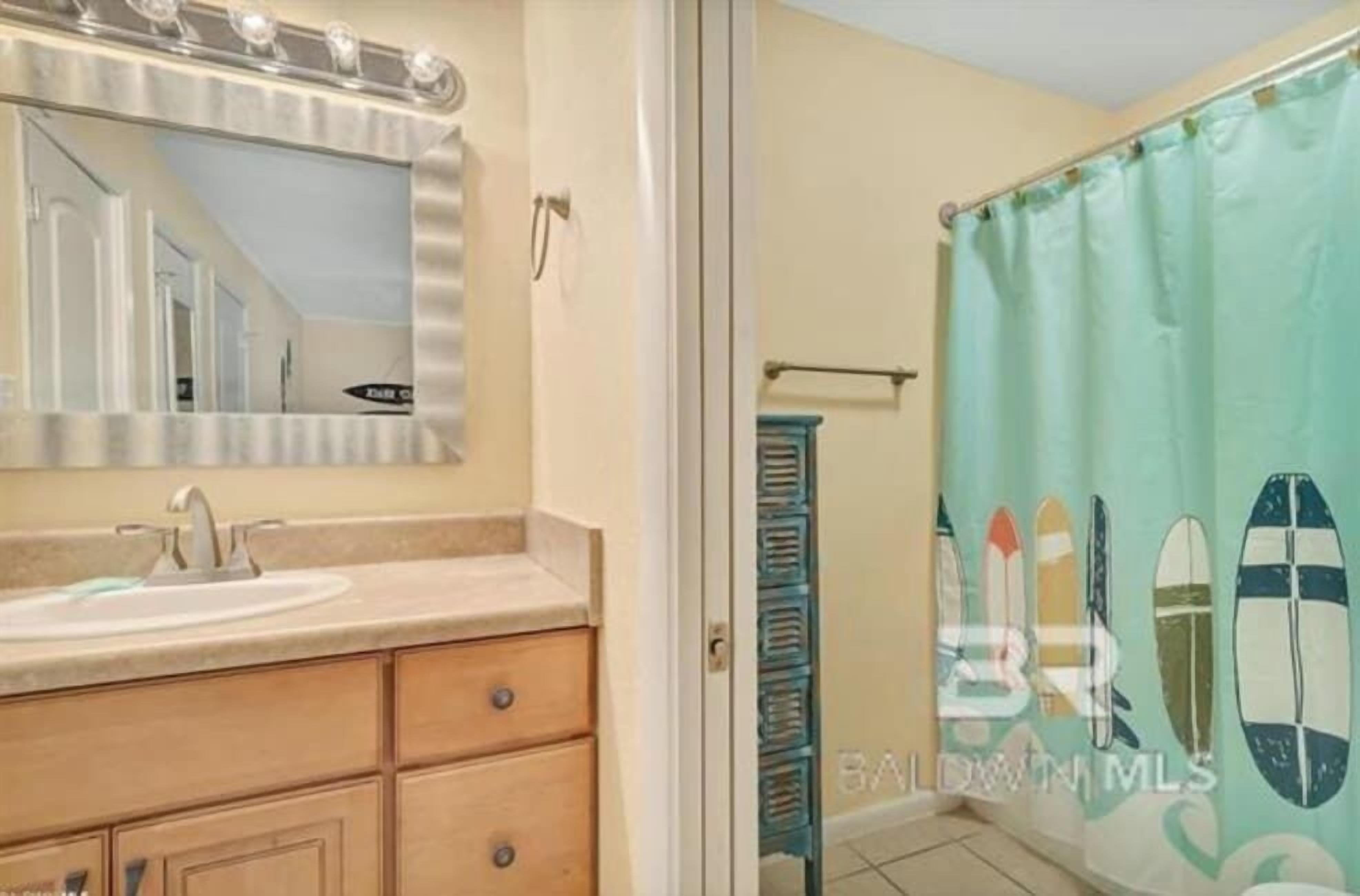 A bathroom with a sink, mirror, and shower curtain with surfboard designs.