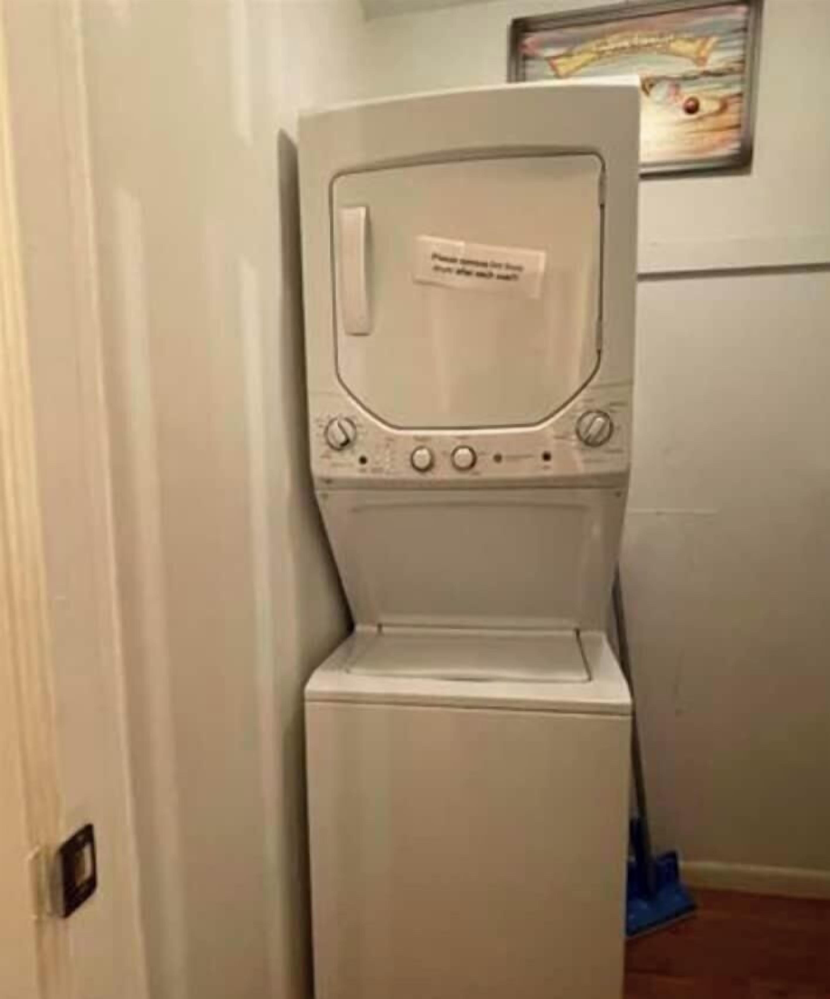 Un appareil compact, blanc, combinant une machine à laver et un sèche-linge à chargement frontal, avec un panneau de commande situé sur le dessus.
