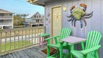 A porch with green Adirondack chairs and a small table, a crab mural on the wall, and a view of neighboring houses.