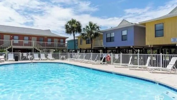 Piscina com espreguiçadeiras e área cercada, em volta de edifícios coloridos.