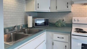 A kitchen with white cabinets, a stainless steel sink, a microwave, and a stove. - Pet Friendly Beach Access Sleeps 6 Hangout Nearby (Gulf Shores)