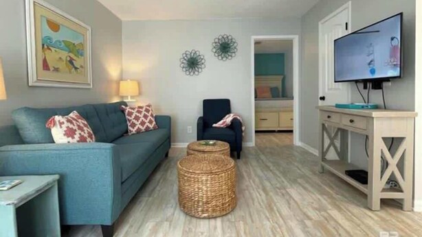 A living room with a blue sofa, a chair, a TV, and a small table. - Pet Friendly Beach Access Sleeps 6 Hangout Nearby (Gulf Shores)