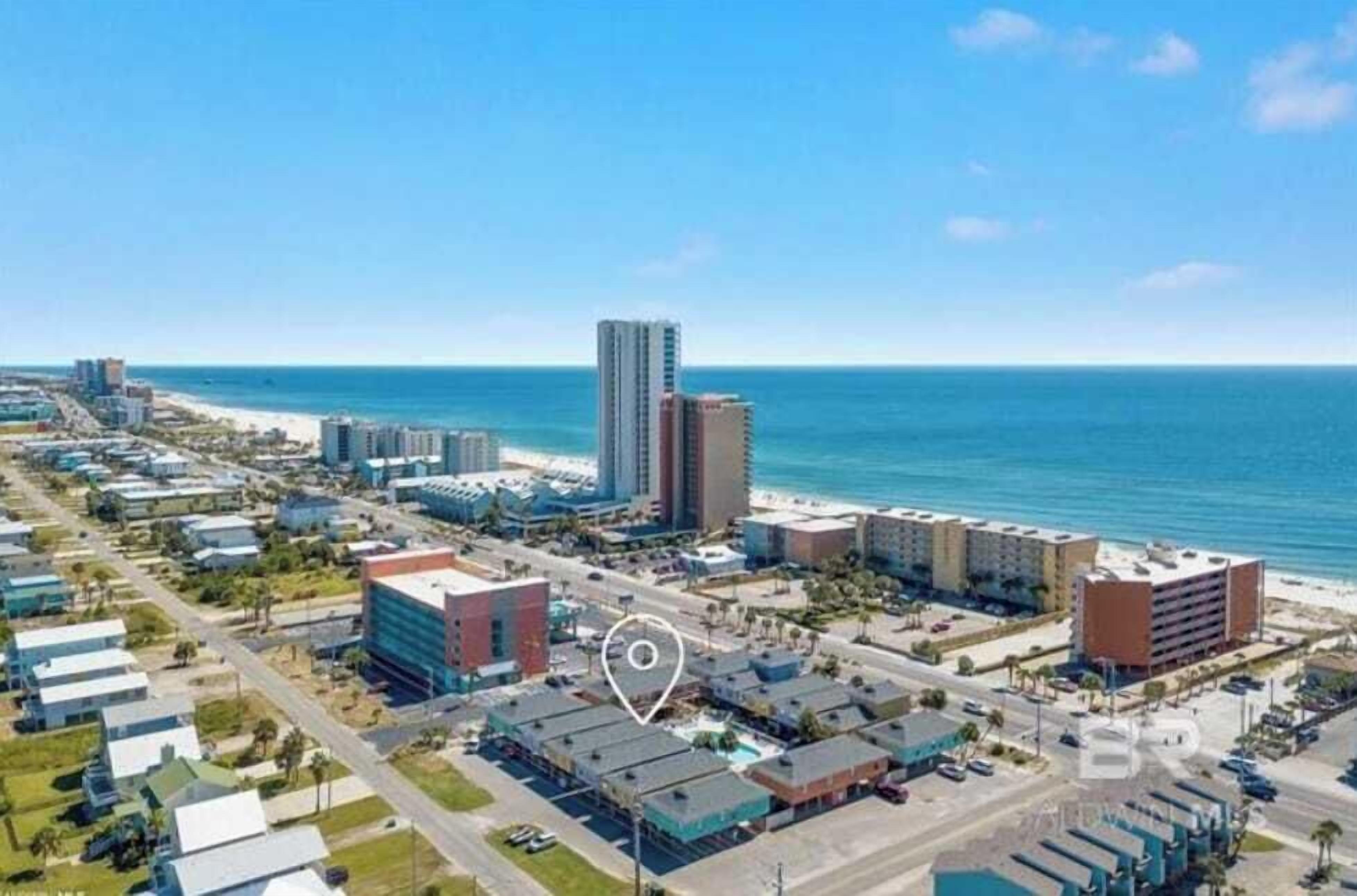 An aerial view of a coastal city with a prominent tall building, a beach, and a mix of commercial and residential buildings.
