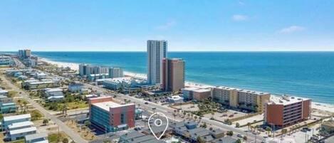 An aerial view of a coastal city with a prominent tall building, a beach, and a mix of commercial and residential buildings.