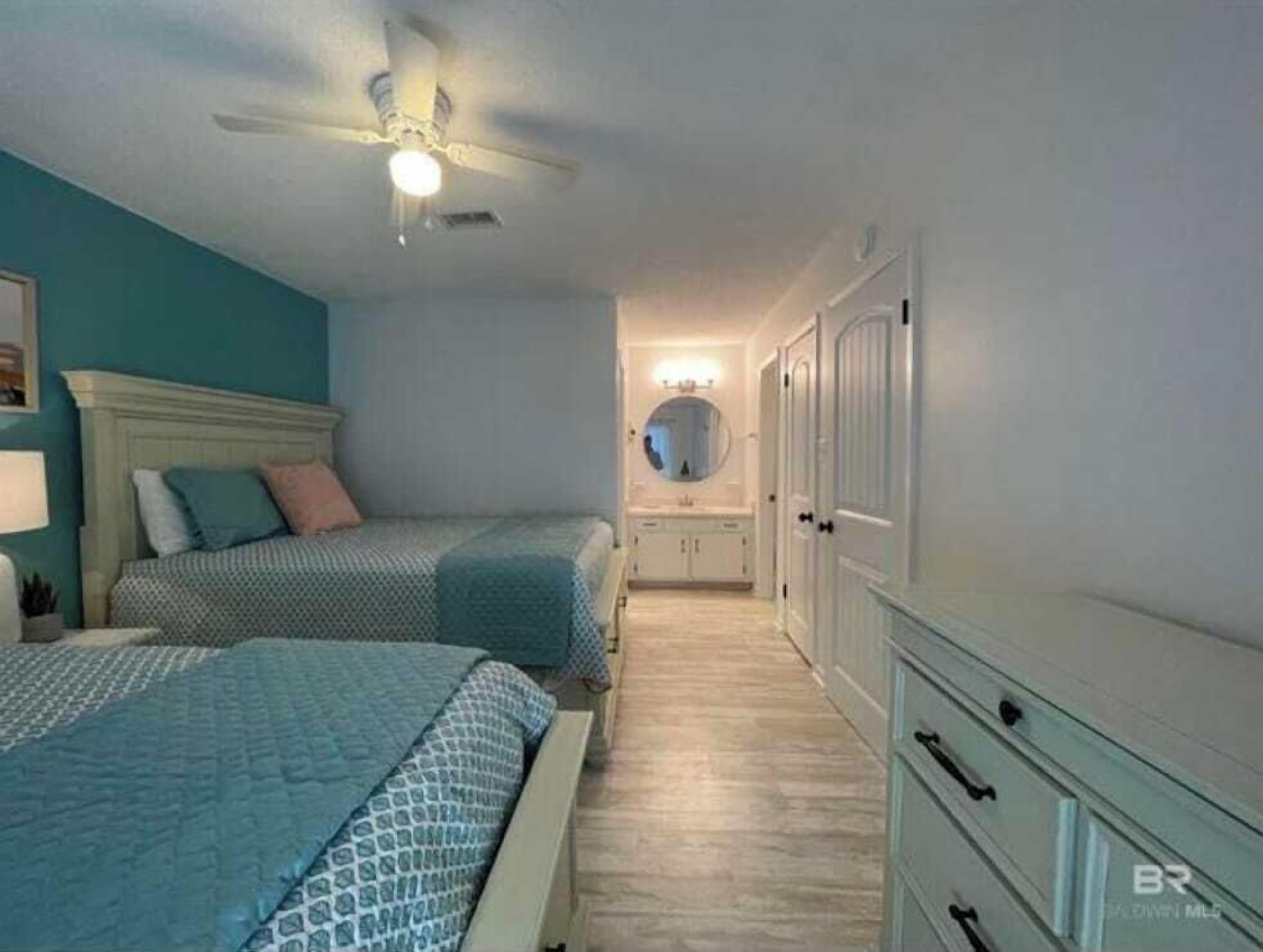 Een slaapkamer met twee bedden, een plafondventilator, een spiegel en een inloopkast.
