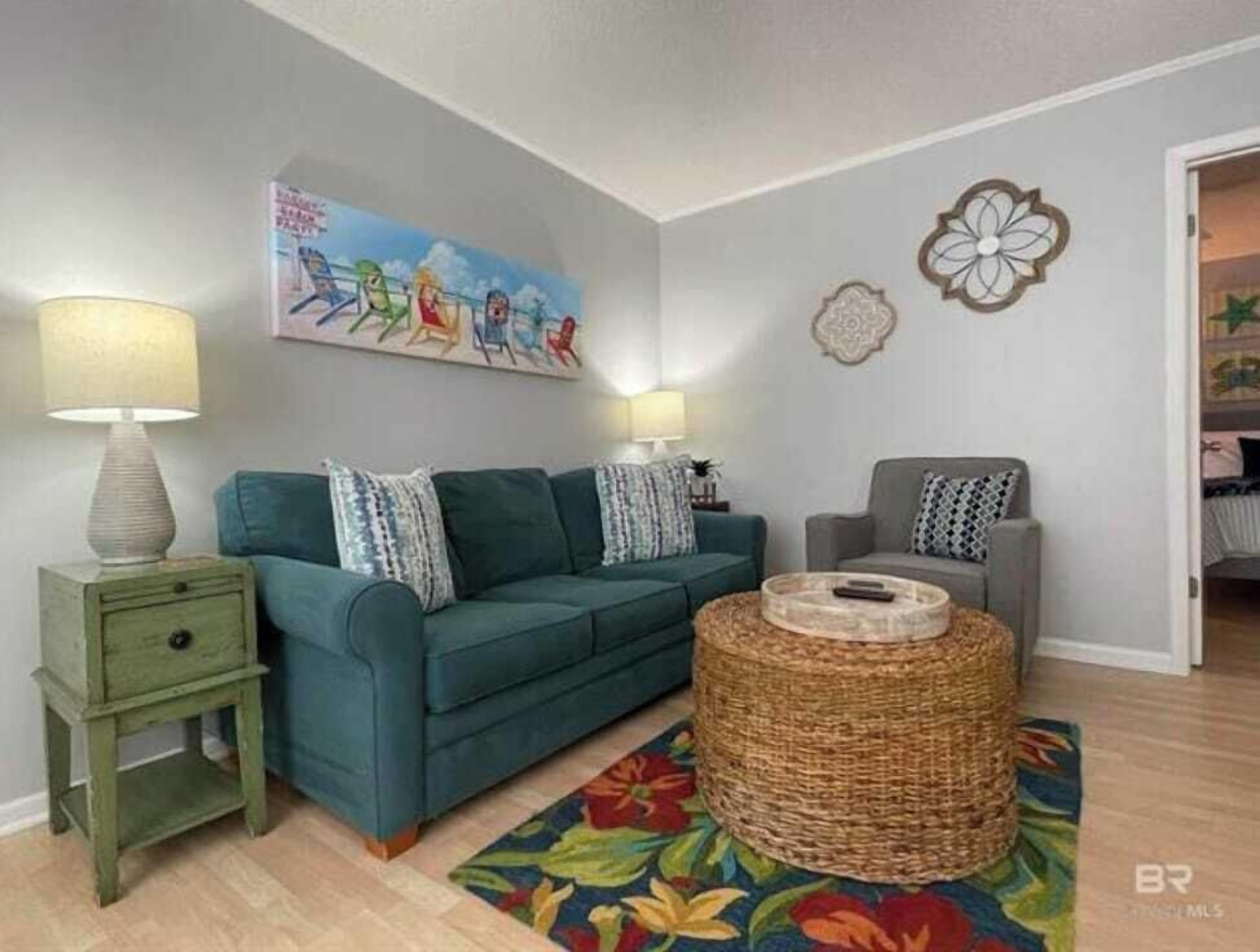 A living room with a teal sofa, two side tables with lamps, a wicker coffee table, and a colorful rug.