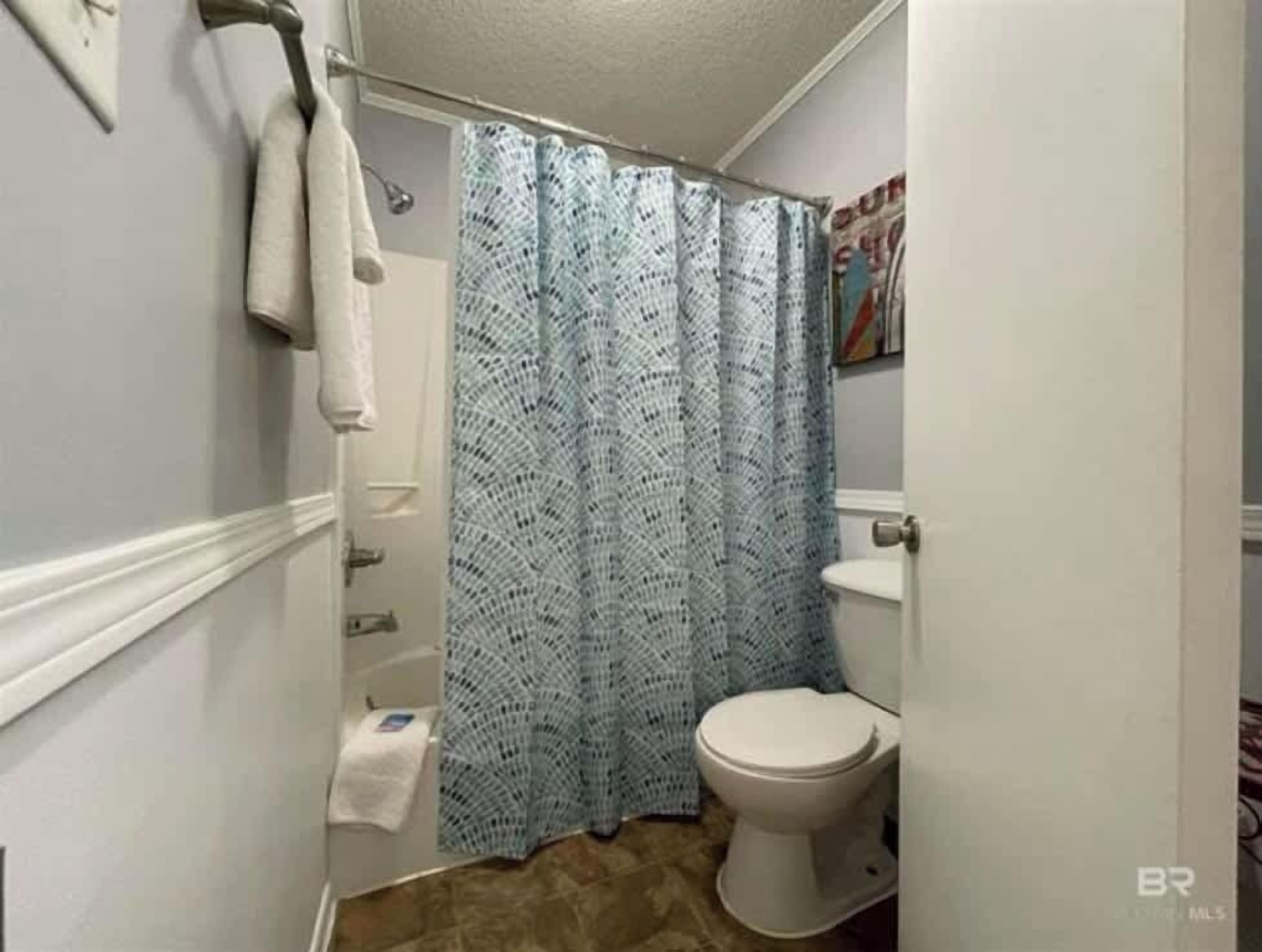 Een kleine badkamer met een wit toilet, een blauw douchegordijn en een handdoek aan een rek.