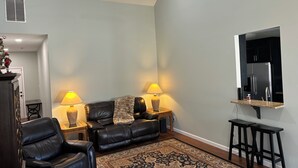 A living room with a black leather sofa, two side tables with lamps, a patterned rug, and a kitchen area with a refrigerator. - Master’s Rental - 2 weeks 3 bed/2bath - 3 miles from golf course Augusta, GA (Augusta)