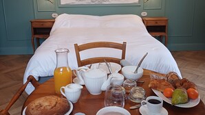 A neatly made breakfast table with a variety of food and drink items, a bed with white linens, and a large wall painting of trees. - Guest House Manoir de Salleviale Conques en Rouergue Aveyron (Conques-en-Rouergue)