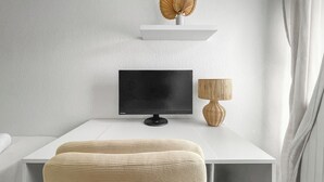 Une pièce moderne et minimaliste, avec un bureau blanc, un écran noir, une chaise en osier et une lampe.