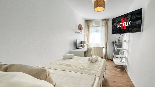 Une chambre d’hôtel avec deux lits, un téléviseur fixé au mur, un bureau et une fenêtre avec des rideaux.