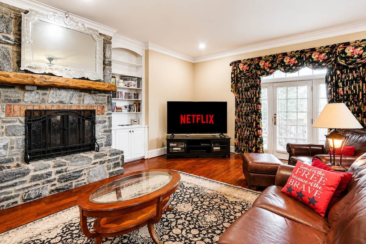 A living room with a stone fireplace, a flat-screen TV, leather sofa, and a patterned rug.