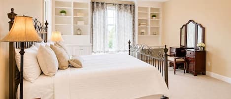 A bedroom with a bed, bedside lamps, a dresser, a mirror, and built-in shelving.
