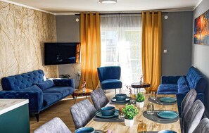 A modern living room with a blue sofa set, a dining table with blue plates, and a TV mounted on the wall. - Beautiful home in Moravice with sauna (Moravice)