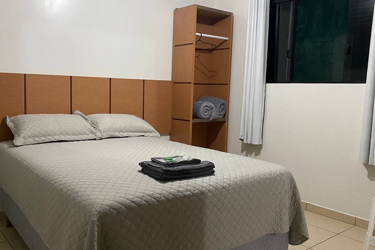 Un lit bien fait, avec une couvre-lit matelassé, une tête de lit en bois et une petite armoire avec une tringle pour suspendre les vêtements.