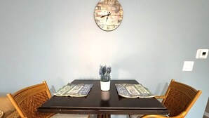 Ruokapöytä, jossa on neljä punottua tuolia, ruukkukasvi ja seinäkello.