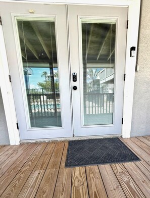 Puerta doble con panel de vidrio y cerradura electrónica, que da a una terraza de madera.