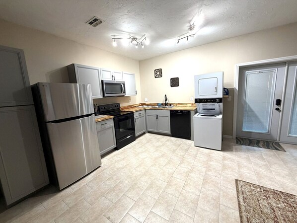 A modern kitchen with stainless steel appliances, grey cabinets, and a tiled floor.
