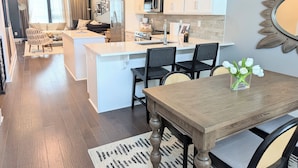 Eine moderne Küche mit weißen Schränken, einer zentralen Kochinsel und einem Essbereich mit Holztisch und Stühlen.