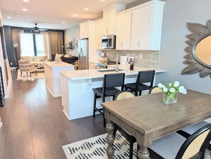 A modern kitchen with white cabinetry, a central island, and a dining area with a wooden table and chairs. - Rooftop Retreat: 3BR/3.5BA, garage, pet friendly, sleeps 8, walk to Uptown (Charlotte)