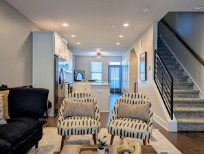 A modern living room with a black sofa, two patterned armchairs, a coffee table with a plant, and a staircase with a black railing. - Rooftop Retreat: 3BR/3.5BA, garage, pet friendly, sleeps 8, walk to Uptown (Charlotte)