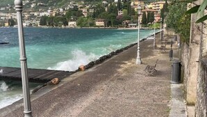 A coastal walkway with a stone pavement, metal lamp posts, and a view of the sea and a hillside town. - Sopri House - Relaxation and Lake View, Private Garden and Veranda (Malcesine)