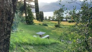 A serene outdoor setting with a grassy area, a stone bench, and a view of a lake and mountains in the background. - Sopri House - Relaxation and Lake View, Private Garden and Veranda (Malcesine)
