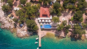 Vue aérienne d’une propriété située sur la côte, avec une piscine, un quai avec des bateaux et des arbres environnants.