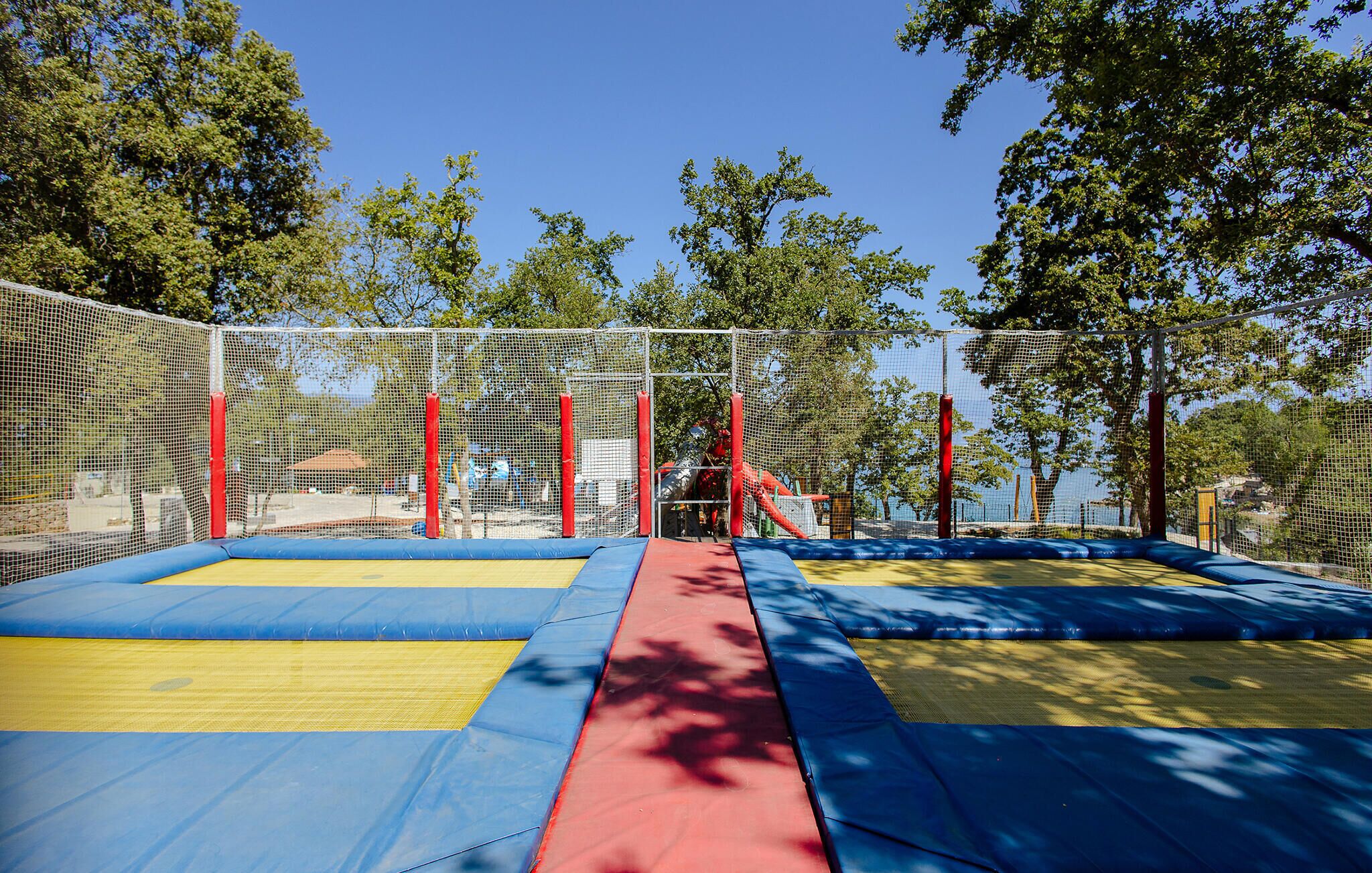 Un parc de trampolines entouré d’un filet de sécurité, avec des arbres en arrière-plan.
