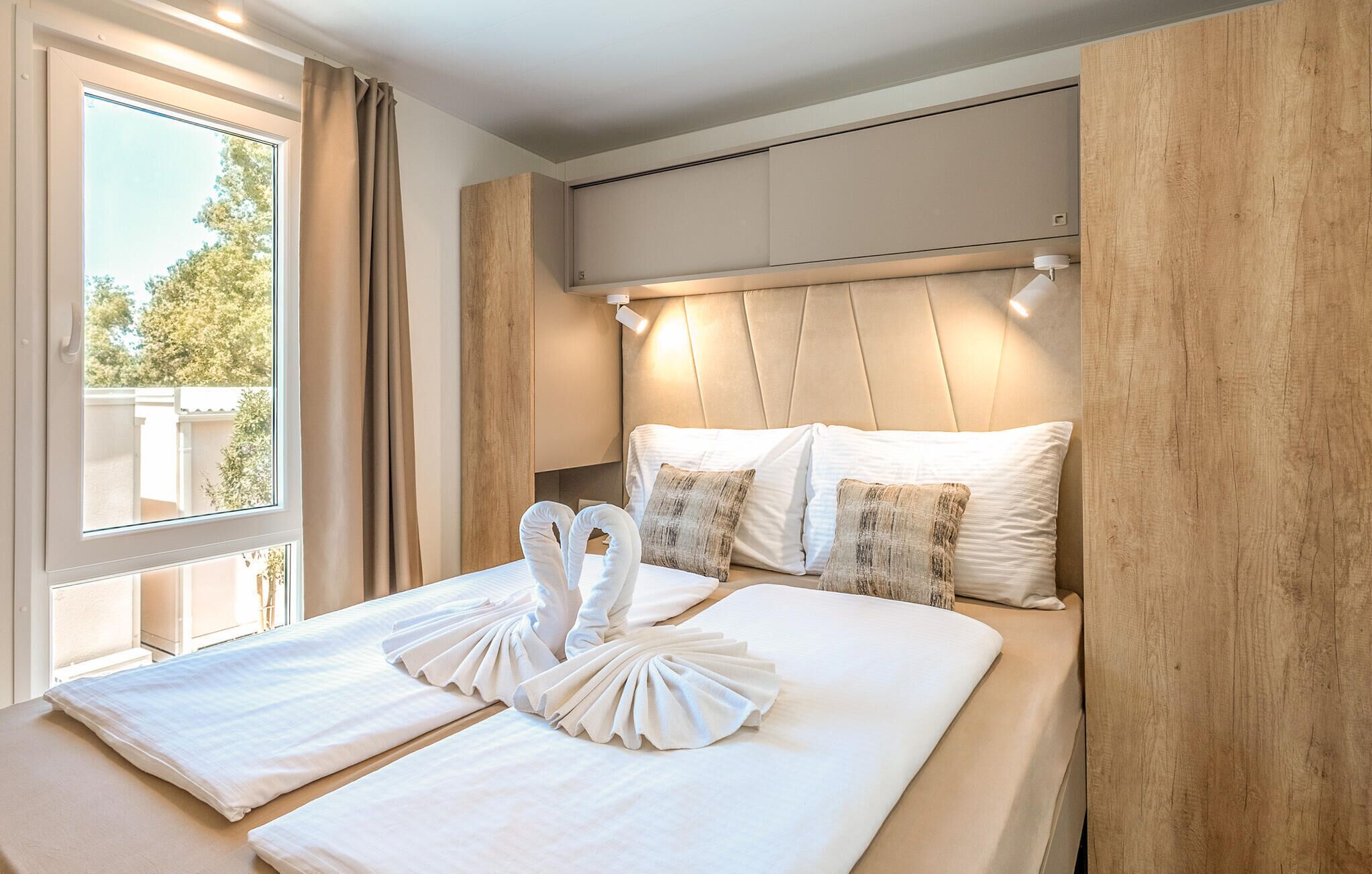 Ein ordentlich bezogenes Bett mit weißen Leinen und einer Handtuchaufstellung, ein Holzkopfstück und ein Fenster mit Vorhängen.