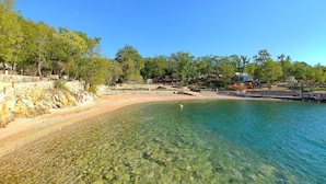 Una playa despejada con un muro de piedra y árboles al fondo.