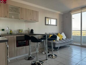 A modern kitchen with a built-in oven, bar stools, and a grey sofa with yellow pillows. - Moderno departamento en Quilpué (Quilpué)