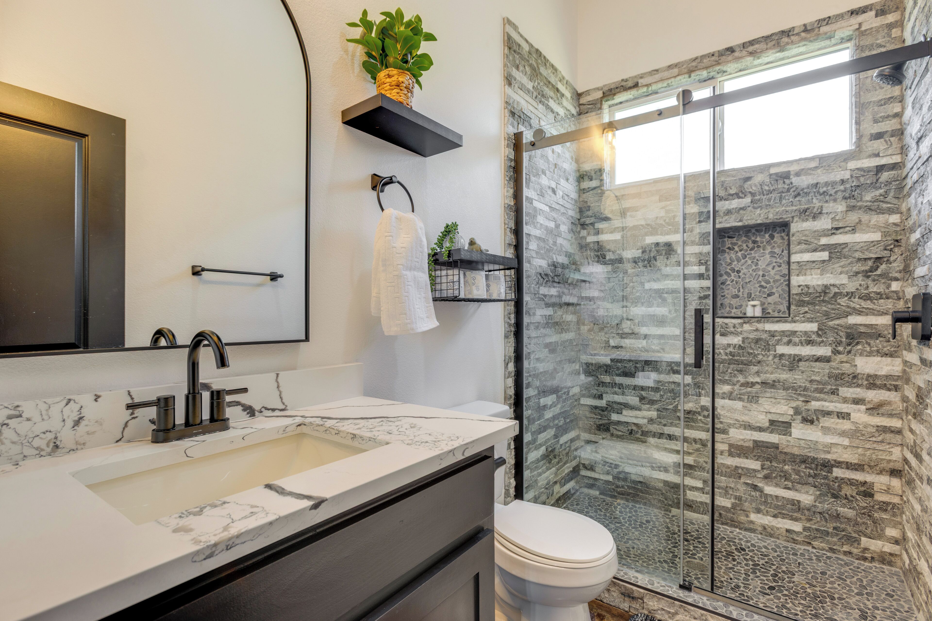 A modern bathroom with a marble sink, a glass shower enclosure, and a stone wall.