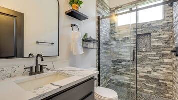 A modern bathroom with a marble sink, a glass shower enclosure, and a stone wall.
