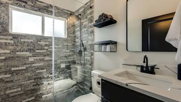 A modern bathroom with a glass-enclosed shower, a white toilet, a black sink with a marble countertop, and a large mirror.