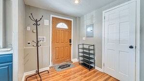 Un couloir avec une porte en bois, un porte-manteau, une étagère en métal et un paillasson.