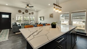 A modern kitchen with a large island, dark cabinetry, and a ceiling fan. - ‘Roo's Hideaway’ Modern 3BR Near Round Top & A&M! (Somerville)