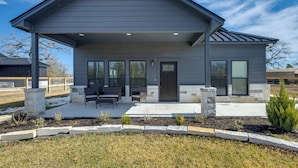 A modern two-story house with a covered patio, stone pillars, and a landscaped garden. - ‘Roo's Hideaway’ Modern 3BR Near Round Top & A&M! (Somerville)