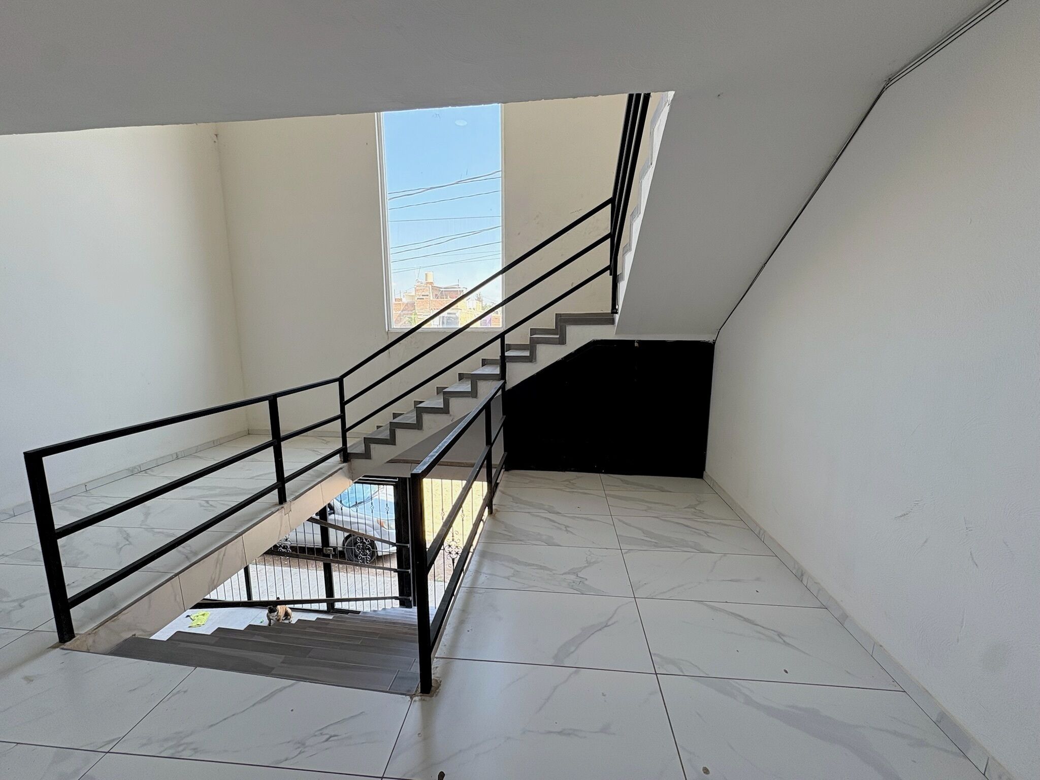 A staircase with a metal railing leading to an upper floor. The floor is tiled with a marble pattern.