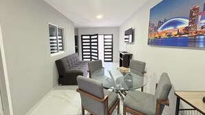 Un salón moderno con una mesa de comedor de vidrio, sofás grises y una pintura de un paisaje urbano.