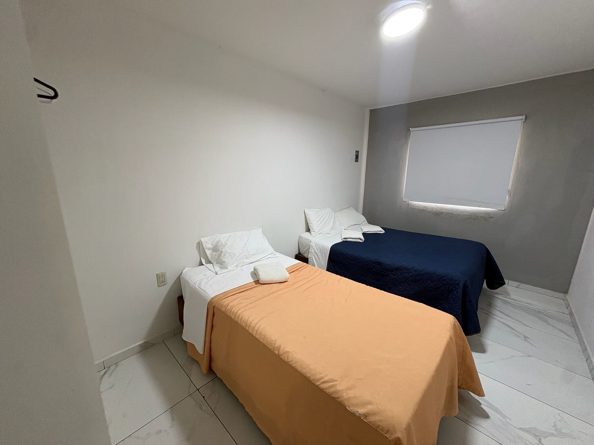 Une petite chambre propre, avec deux lits simples, une fenêtre et un mur blanc.