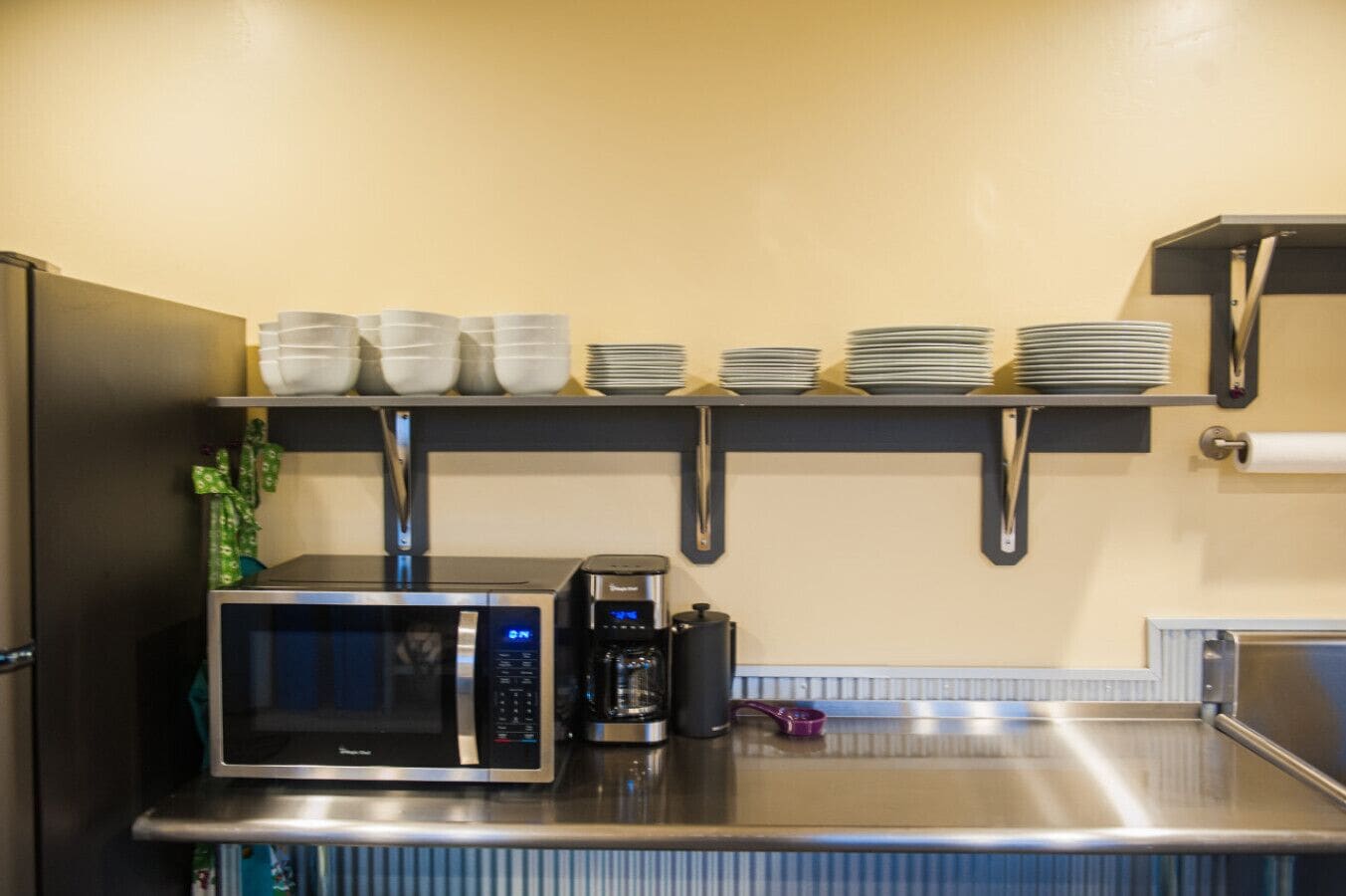 Een keuken met een magnetron, koffiezetapparaat en gestapelde borden op planken.