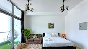 Et moderne soveværelse med en stor seng, en sofa, en potteplante og udsigt gennem et stort vindue.
