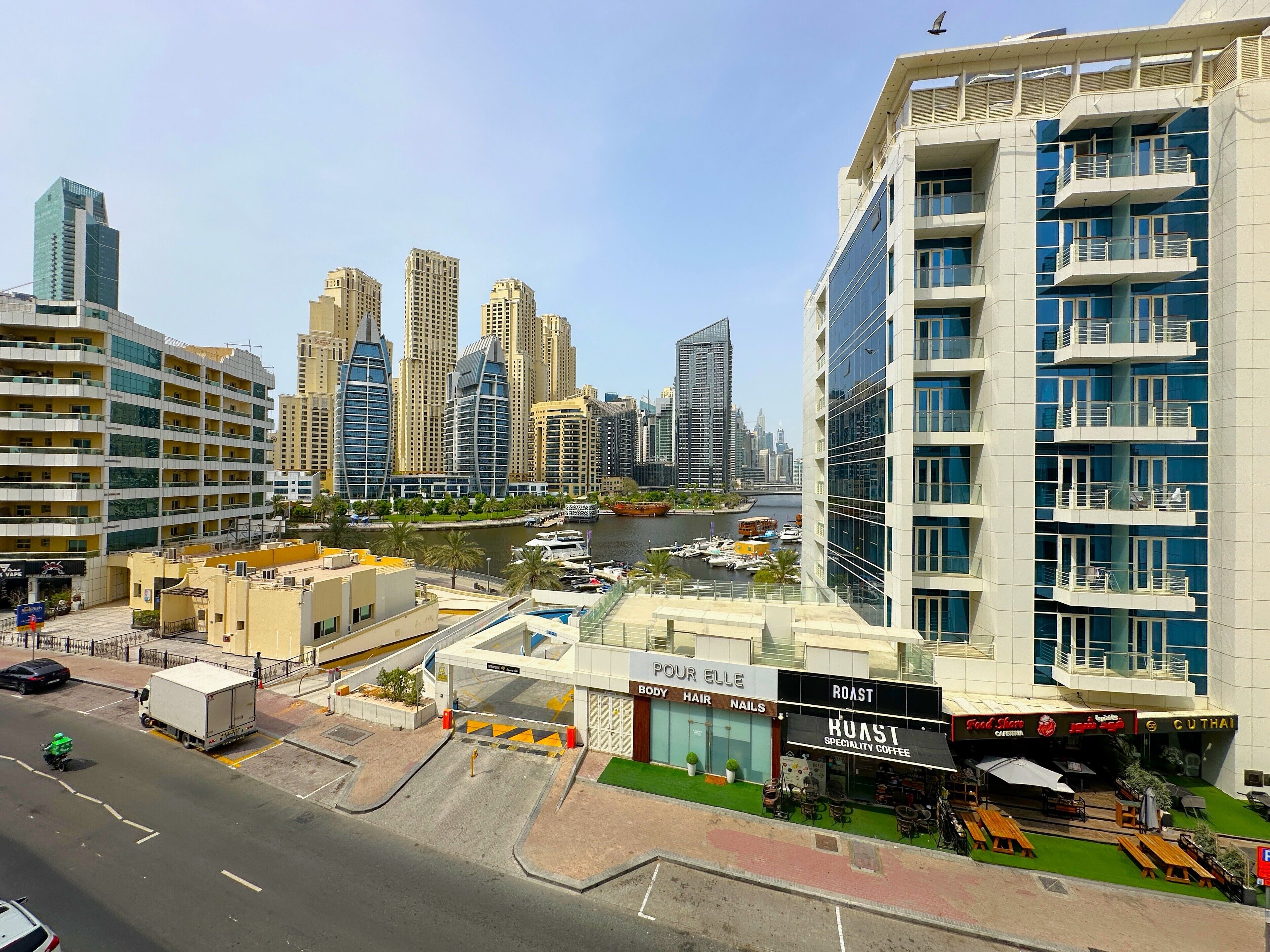 A modern urban area with high-rise buildings, a marina with boats, and a coffee shop named Roast Specialty Coffee.
