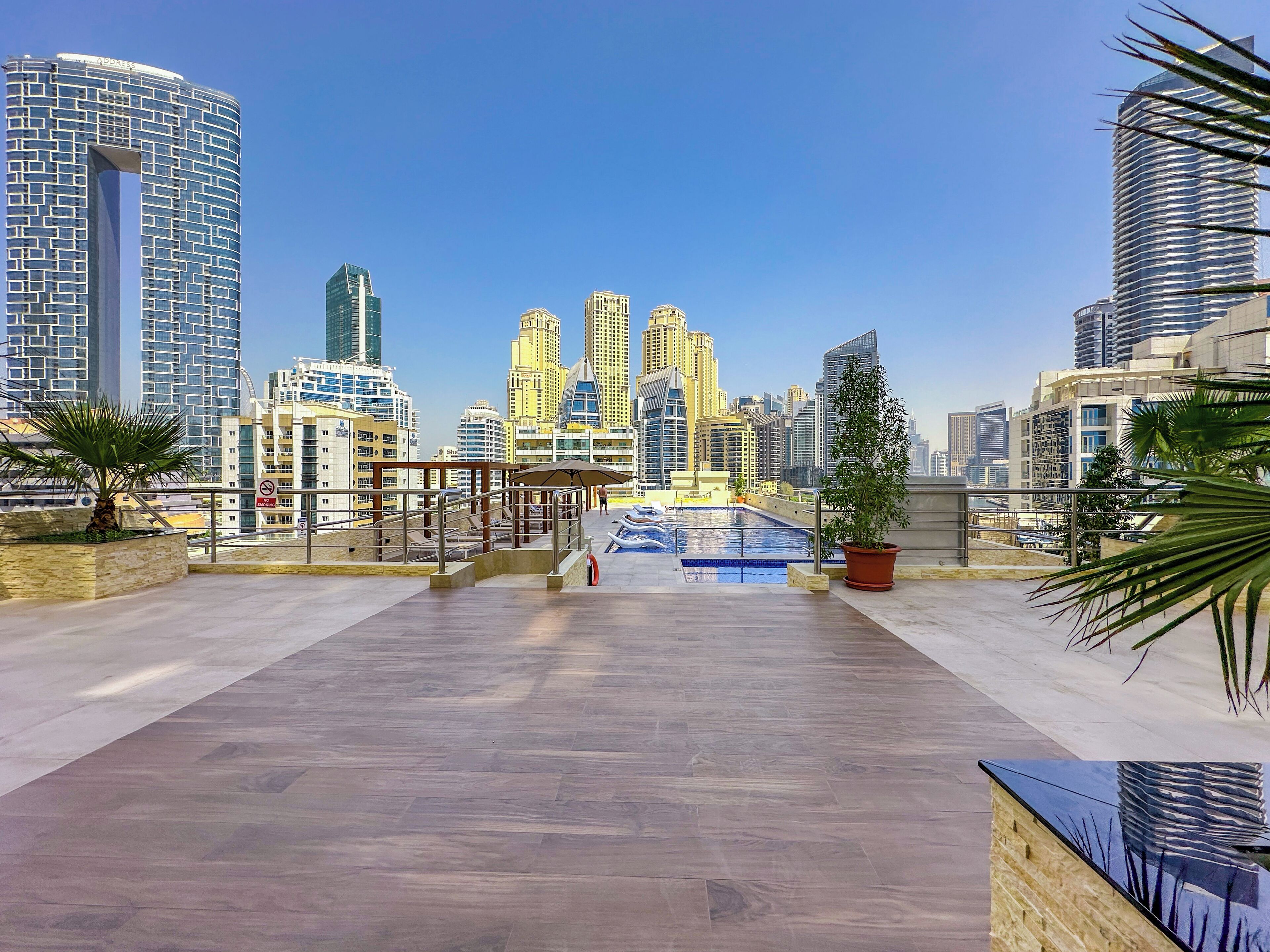 Eine Dachterrasse mit Pool, Palmen und einer Stadtkulisse im Hintergrund.