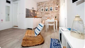 Un soggiorno moderno con una parete in pietra, un divano bianco con un cuscino a righe, un pavimento in legno e un'area pranzo con tavolo e sedie.