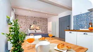 Una cucina moderna con una parete in pietra, un tavolo da pranzo apparecchiato per la colazione, e vista su una camera da letto con un letto e una sveglia.
