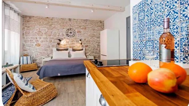 Una camera da letto con una parete in pietra, un letto, un comodino in legno con arance e una parete decorata con un motivo blu.